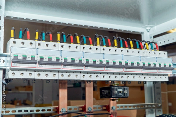 Obraz A range of electrical wires or cables are connected to the modular circuit breakers. Black wires are marked in different colors. In the background, the design of the electrical Cabinet with busbars.