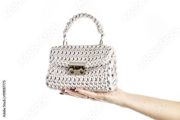 Fototapeta Kobieta za rękę trzyma małą szydełkową torebkę w kolorze beżowym na białym tle.
