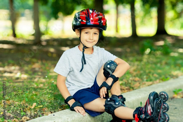 Fototapeta Little boy riding on rollers in the summer in the Park. Happy child in helmet learning to skate.