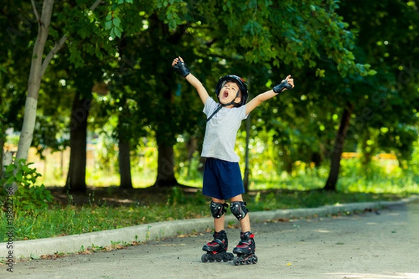 Fototapeta Little boy riding on rollers in the summer in the Park. Happy child in helmet learning to skate. Victory in the competition.