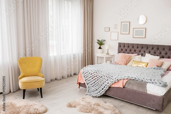 Fototapeta Comfortable bed and tropical plant with green leaves in room interior
