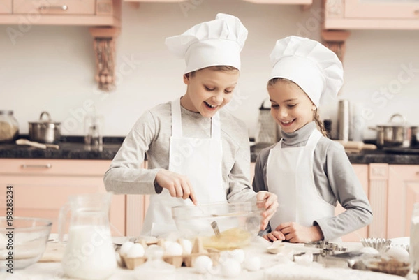 Fototapeta Children in kitchen. Brother and sister are whisking eggs with fork.