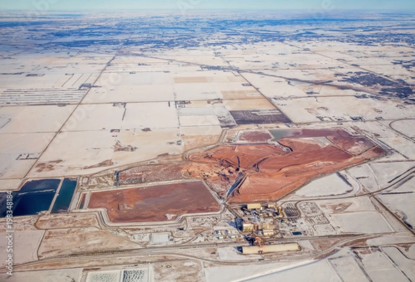 Fototapeta A potash mine surrounded by patchwork of agriculture fields and winding roads viewed from an airplane in a winter landscape in saskatchewan