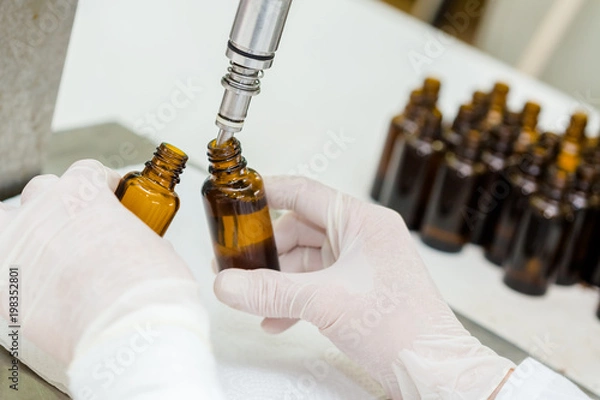 Fototapeta Close up of female lab worker hand with gloves filling the bottle with syrup