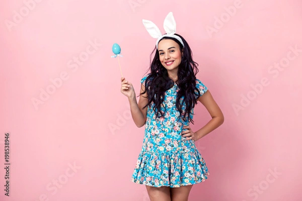 Fototapeta Happy easter! Beautiful sexy young woman wearing bunny ears on Easter day and holding basket with Easter eggs. Pretty girl preparing for Easter.