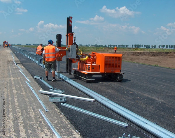 Fototapeta Road worker mounting the roadside guardrail