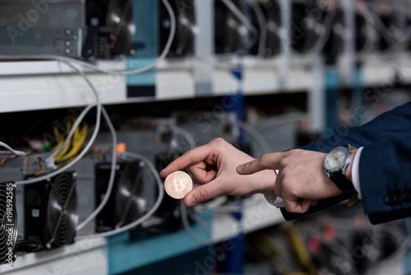 Fototapeta cropped shot of businessman pointing at bitcoin at cryptocurrency mining farm