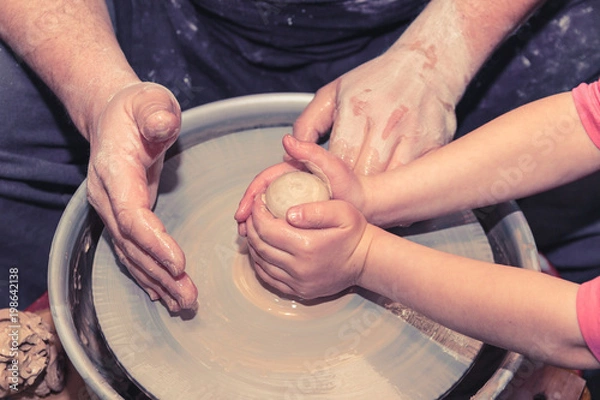 Fototapeta Little child learns how to sculpt a ceramic plate on a potter's wheel. Close-up of a child's hand.
