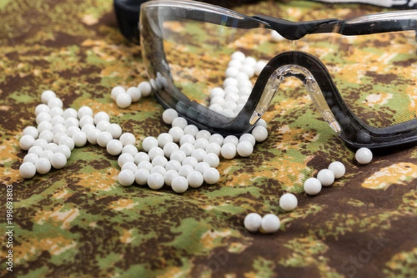 Fototapeta balls airsoft bbs and protective glasses on a camouflage background