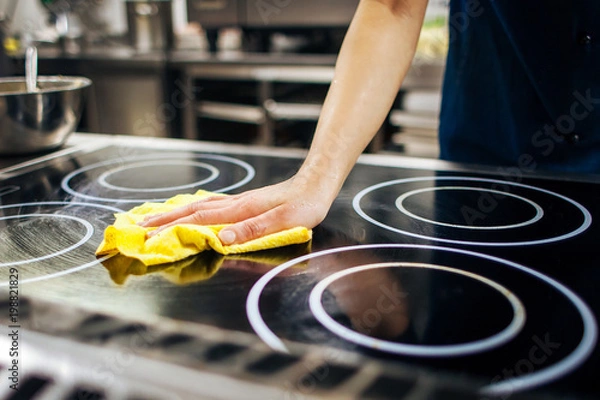 Obraz chef wipes the kitchen stove with a napkin