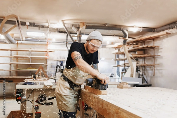 Obraz Carpenter working with electric planer on wooden plank in workshop. Craftsman makes own successful small business.