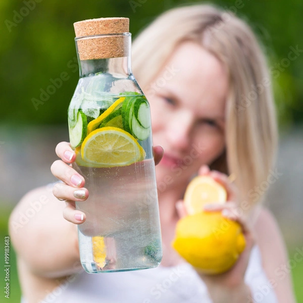Fototapeta healthy eating, drinks, diet. The girl is holding a detox drink from a lemon and mint with a cucumber on a background of green grass