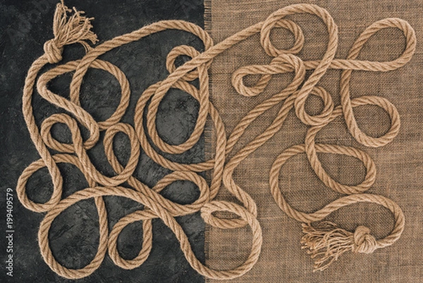 Fototapeta flat lay with brown marine ropes with knots on sackcloth and dark concrete surface