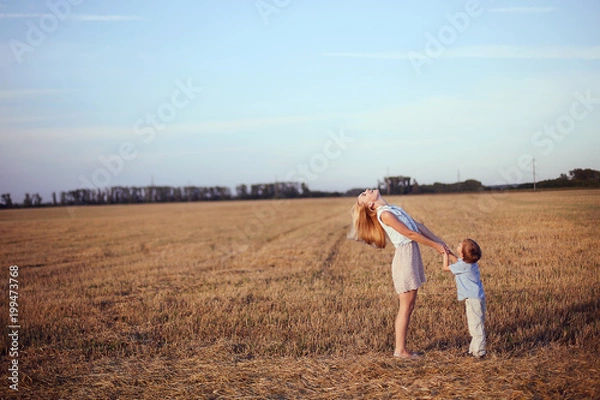 Obraz Young blonde beautiful mother walking with her smiling son on the golden field. Happy family and sunny day