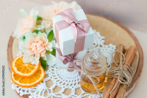 Obraz Made at home from orange oil with cinnamon perfume in a glass jar. Slices of dried orange, dried cinnamon and flowers. Gift box with jewelry charm bracelet is on the table. Present for every woman.