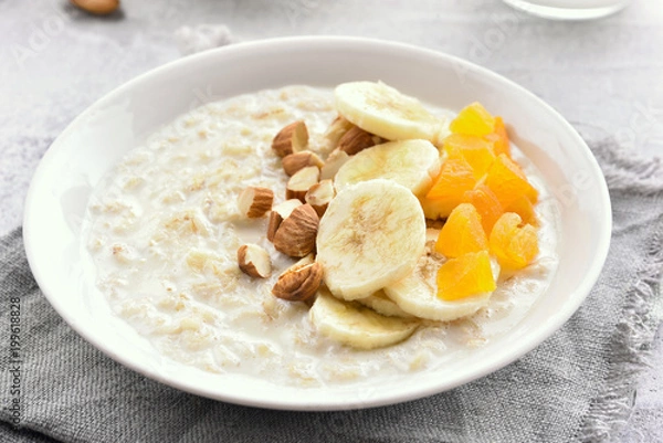 Fototapeta Oatmeal porridge with banana slices, nuts and dried apricot