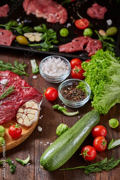 Fototapeta Flat lay of raw beefsteak with vegetables, herbs and spicies on metal tray, close-up, selective focus