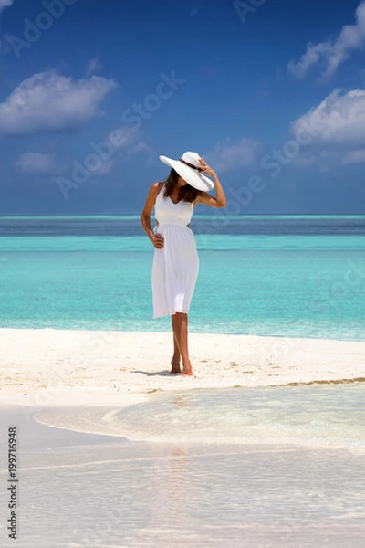 Fototapeta Frau in weißem Kleid steht auf einer tropischen Sandbank vor türkisem Meer und blauem Himmel auf den Malediven