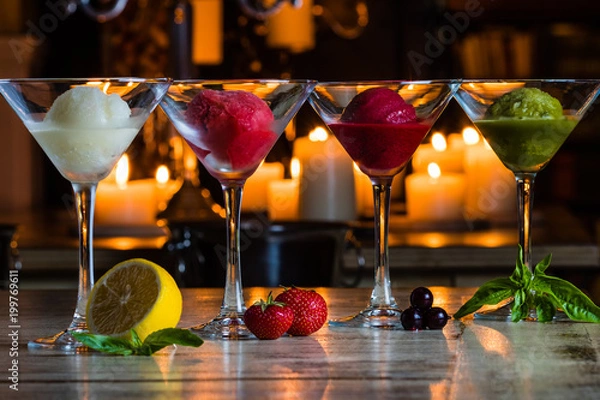 Fototapeta Four kinds of natural colourful sorbet decorated by lemon, mint, strawberry, blueberry and basil in front of candles on the bar counter. Natural ice cream