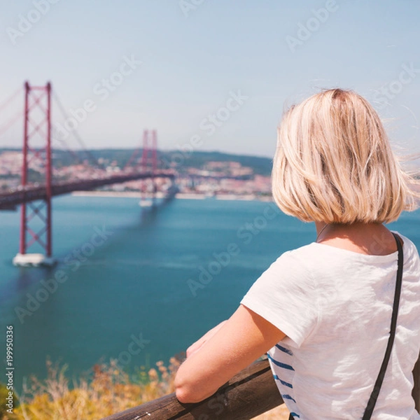 Fototapeta Female traveler standing next to the statue of National Sanctuary of Christ the King and enjoys panoramic views of Lisbon and the bridge of April 25.