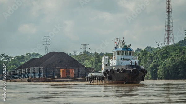 Fototapeta tugboat pulling heavy loaded barge of black coal in the Mahakam river, Indonesia