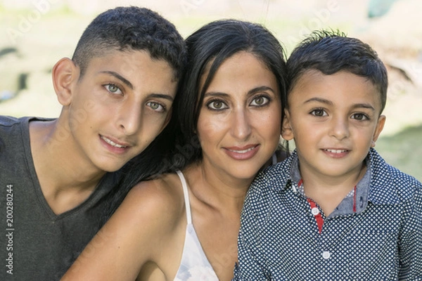 Obraz Outdoor portrait of a smiling mother and her sons. Attractive brunette mother and two brothers smiling in garden.