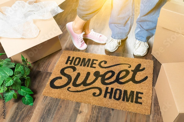 Fototapeta Mężczyzna i kobieta stojący w pobliżu domu Sweet Home Welcome Mat, ruchome pudełka i rośliny