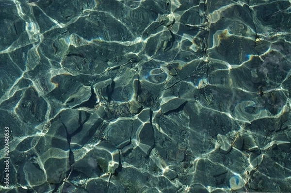 Obraz Horizontal photo of cristal clear water with rocks and sand at the bottom and sunlight reflections