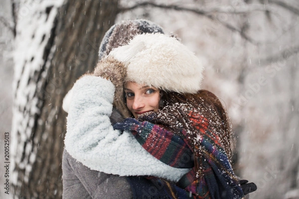 Fototapeta Side view of the happy young couple who is standing in the embrace in the snow-covered park