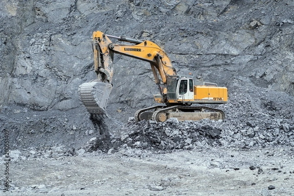 Fototapeta Crawler excavator Liebherr while working out on the quarry, against the backdrop of a rocky slope