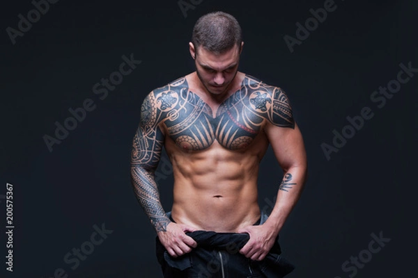 Obraz The man with a muscular naked torso with tattoos on the dark background. ABS