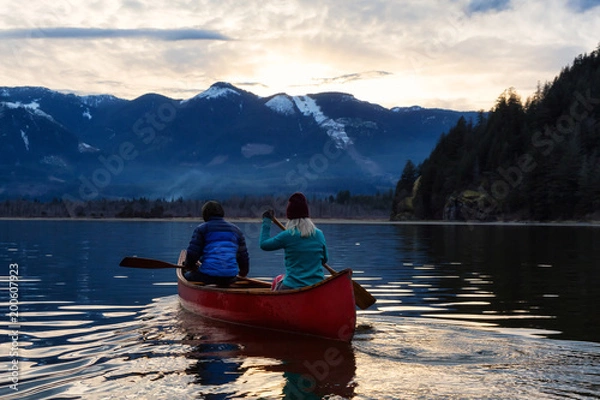 Fototapeta Adventurous people on a wooden canoe are enjoying the beautiful Canadian Mountain Landscape during a vibrant sunset. Taken in Harrison River, East of Vancouver, British Columbia, Canada.