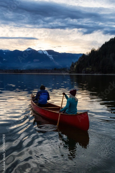 Fototapeta Adventurous people on a wooden canoe are enjoying the beautiful Canadian Mountain Landscape during a vibrant sunset. Taken in Harrison River, East of Vancouver, British Columbia, Canada.