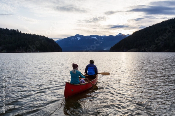 Fototapeta Adventurous people on a wooden canoe are enjoying the beautiful Canadian Mountain Landscape during a vibrant sunset. Taken in Harrison River, East of Vancouver, British Columbia, Canada.