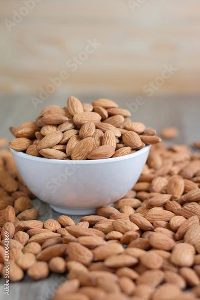 Obraz Pile of almonds nut in a while bowl against wooden background select focus shallow depth of fieldPile of almonds nut in a while bowl against wooden background select focus shallow depth of field