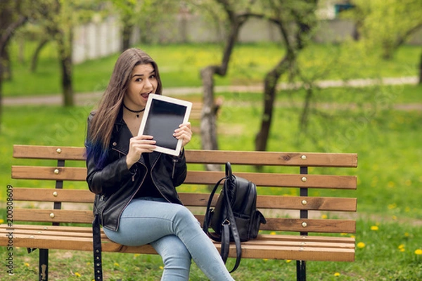 Fototapeta Portrait of young girl holding digital tablet in the park