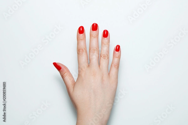 Fototapeta Female palm with red nails painted on a white background