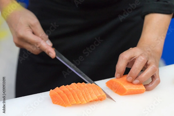 Obraz Hand of chef use knife preparing a fresh salmon on a cutting board, Japanese chef in restaurant slicing raw salmon, ingredient for seafood dish