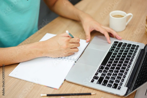 Obraz close up man hand writing something on notebook and playing laptop in free time , lifestyl people concept
