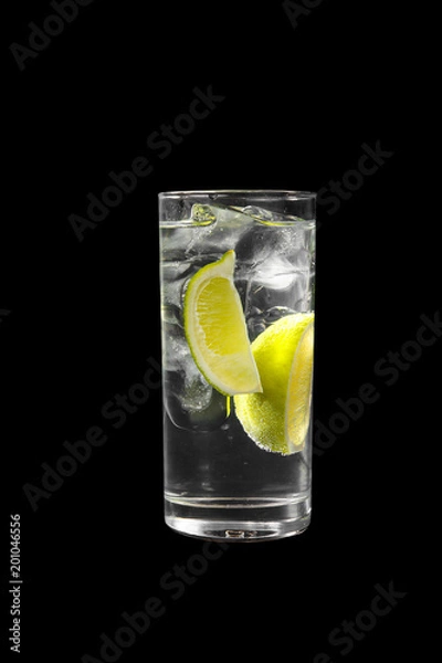 Obraz Transparent cocktail in a tall glass with ice cubes with two slices, lime quart, soda, aeration. Side view Isolated black background. Drink for the menu restaurant, bar, cafe