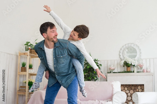 Fototapeta Wspaniały ojciec to taki, którego dzieci go podziwiają! Latający chłopiec siedzący na plecach ojca z wielką przyjemnością spędza wolny czas.
