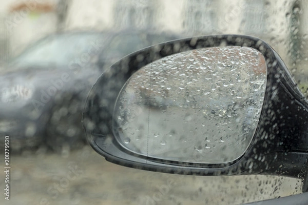 Fototapeta Drops of rain on the car window (glass) with a view of the exterior mirror and blurred background