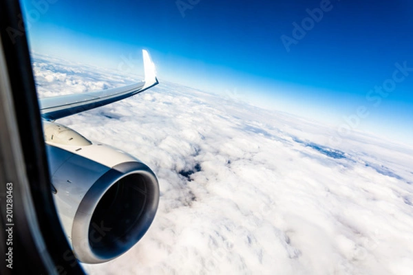 Fototapeta On a plane, looking out of the window above the clouds, the wing is visible and the jet engine