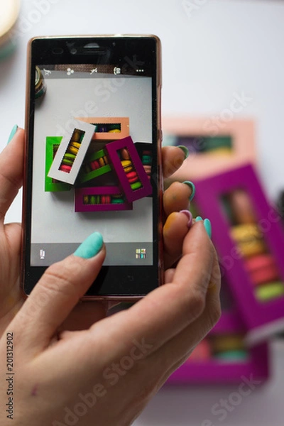 Fototapeta photo in the phone of macaroons in colored boxes