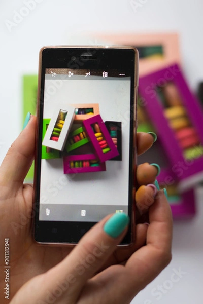 Fototapeta photo in the phone of macaroons in colored boxes