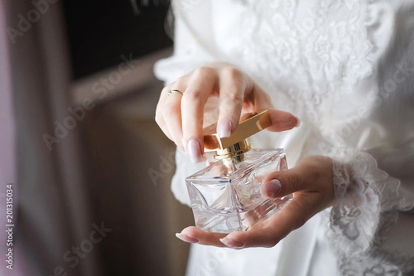 Obraz Close up photo of a luxury perfume flacon being opened in manicured hands of elegant bride wearing white dressing gown