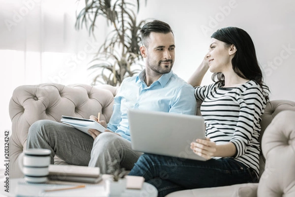 Fototapeta Love during work. Pleasant gay two colleagues looking at each other while working and posing on sofa