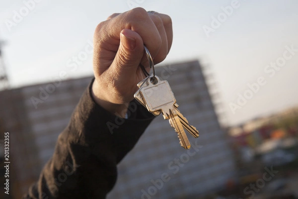 Obraz Mano de mujer sujetando unas llaves. Edificio en obras fuera de foco al fondo.