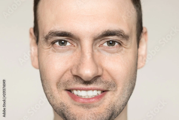 Obraz Handsome young man with a bristle smiling teeth. Portrait of a guy in a gray shirt on a light background.
