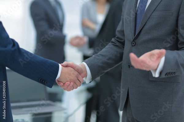 Fototapeta Business partners handshaking over business objects on workplace